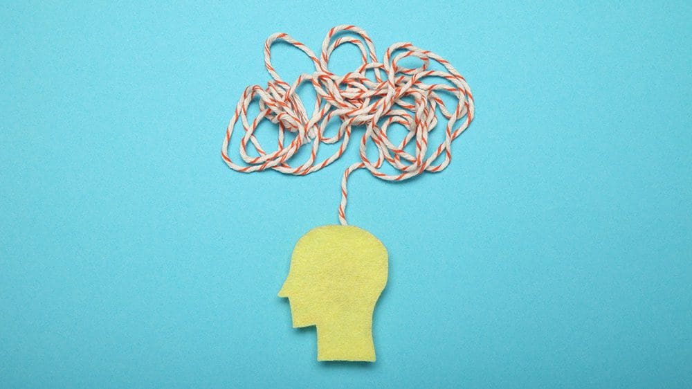 Paper cutout of human head with string coming out of it and tangled above the head to represent confusion