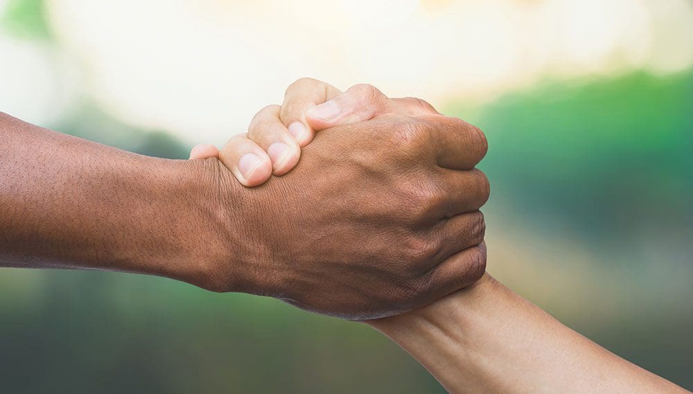 Closeup of two hands in classic pose of one person helping another stand up